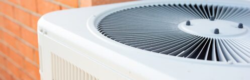 A view of an air conditioner condenser unit in the backyard of a home.